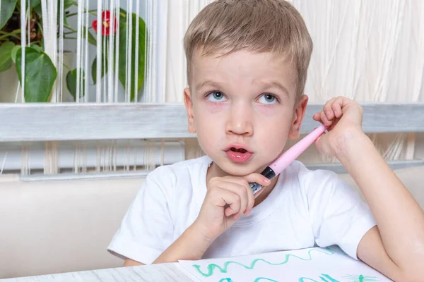 Милый задумчивый маленький мальчик держит в руках ручку с войлоком и думает о рисунке для мамы. Обучение рисованию — стоковое фото