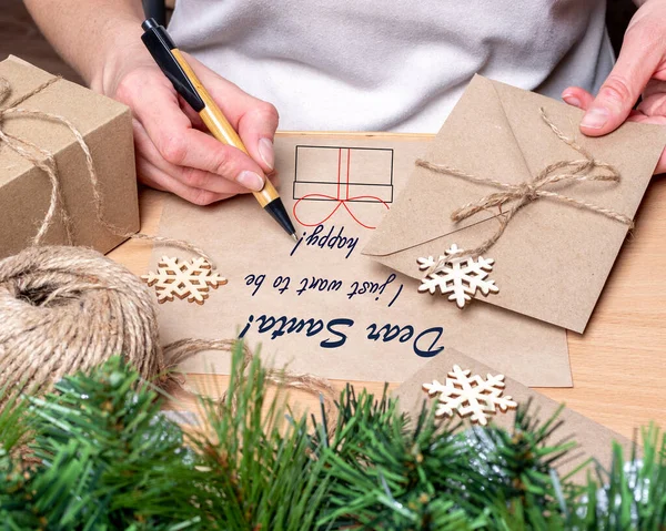 Una mujer le pide felicidad a Santa. Mujer escribiendo una carta de Navidad a Santa Claus, sosteniendo un sobre sobre sobre la mesa — Foto de Stock