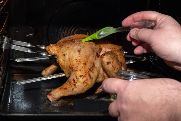 Mains masculines couvrant le poulet entier cru rôti au four avec de la sauce. Préparation d'un plat de viande pour un dîner festif — Photo