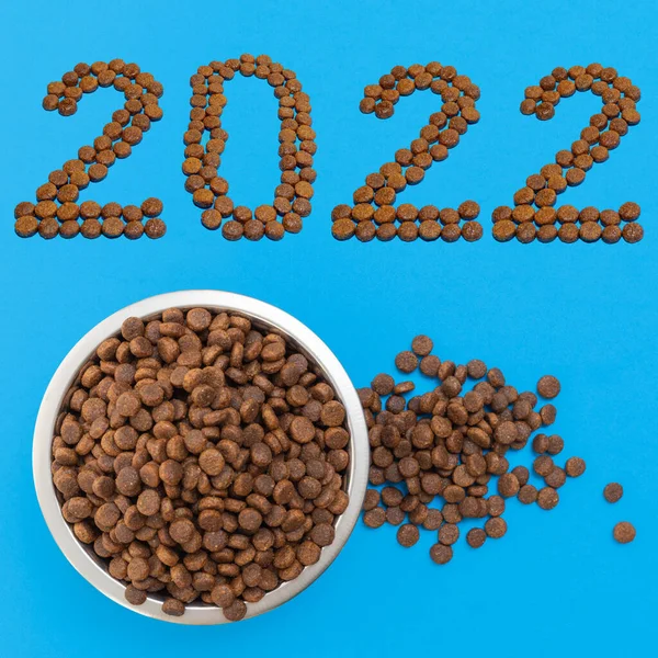 Data 2022 composta por alimentos secos e uma tigela de metal redondo para cães ou gatos cheios de alimentos secos crocantes em um fundo azul — Fotografia de Stock