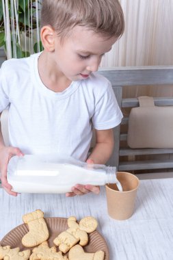 Beyaz tatlı çocuk, Noel Baba 'nın kurabiyelerinin yanındaki masada duran kağıt bardağa süt döküyor. Noel arifesi konsepti.