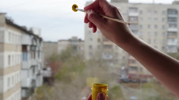 Egy nő keze egy mosolygó arcot fest egy ház ablakára sárga festékkel ecsettel, közelről, Full HD — Stock videók