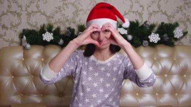 Ben de seni seviyorum. Kırmızı Noel Baba şapkalı ve pijamalı bir kadın yatakta oturmuş sana bakıyor ve elleriyle kalbini gösteriyor..