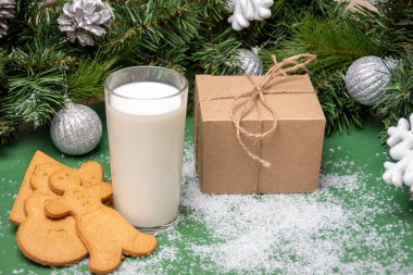 Noel kurabiyeleri, bir bardak süt ve Noel süslemeleri ve köknar dallarıyla dolu bir masanın üzerindeki el sanatları kutusunda bir hediye..