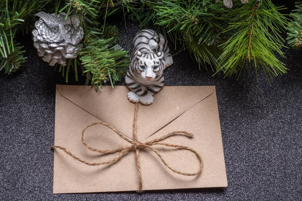 De watertijger is het symbool van het Chinese nieuwjaar 2022. Speelgoedtijger met een ambachtelijke envelop op een grijs glanzende achtergrond met takken van een sparren. Goed nieuws concept — Stockfoto