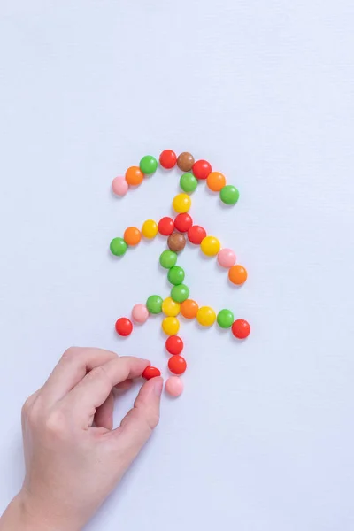 Vertical image a childs hand laying out the shape of a Christmas tree made of colorful candies. Christmas food decor. — Stock Photo, Image