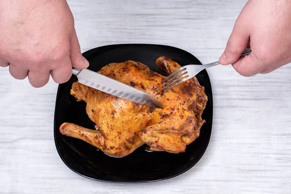 Mains tenant un couteau et une fourchette pour couper le poulet frit sur une assiette noire sur la table. Nourriture traditionnelle de Noël. — Photo