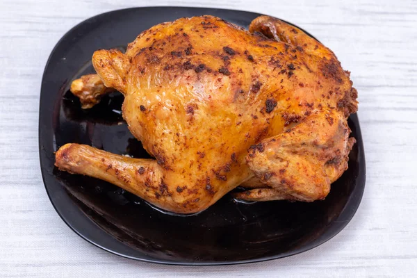 Un poulet frit entier ou de la dinde sur une assiette noire sur la table, vue du dessus. Poulet à la croûte croustillante brune. — Photo