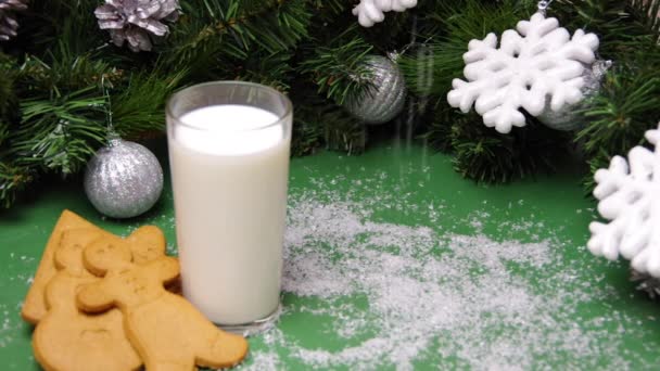 Τεχνητό χιόνι πέφτει σε χριστουγεννιάτικα μπισκότα, ένα ποτήρι γάλα και χριστουγεννιάτικα στολίδια. Χριστουγεννιάτικο δώρο για Santa Full HD — Αρχείο Βίντεο