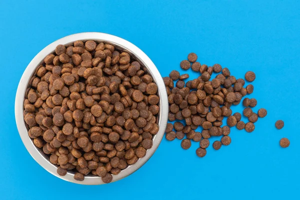 Kulatá kovová mísa plná křupavé suché krmivo pro psy nebo kočky na modrém pozadí. Péče o zvířata. Lahodné a zdravé jídlo — Stock fotografie