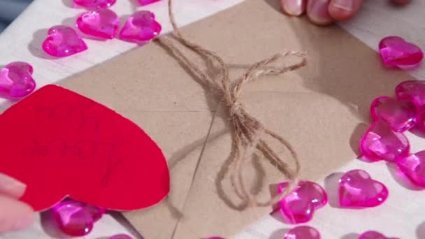 Manos femeninas decorando un sobre de papel y un corazón de papel rojo con la inscripción TE AMO. Envoltura de regalo de San Valentín — Vídeo de stock