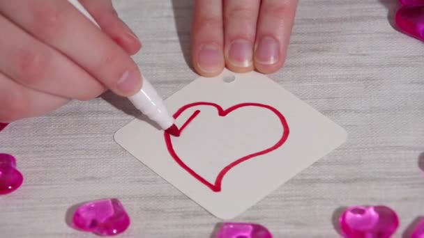 Coloração da mão com linhas como um pulso com um marcador vermelho uma forma de coração em uma folha branca de papel em uma mesa com corações — Vídeo de Stock