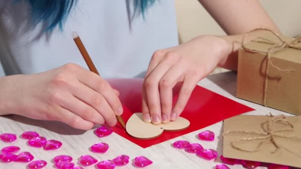 Valentines Day craft DIY. A female hand draws a contour of a heart shape on red paper on a table with gifts and decorations — Stok Video