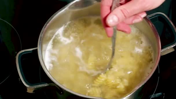 Hand stirring raw pasta boiling in boiling water in a metal pot on the stove, close-up, full hd. Homemade food concept — Vídeo de stock