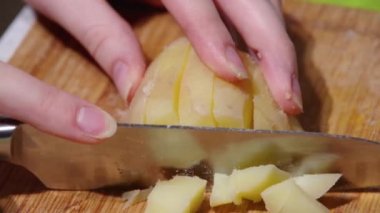 Close-up of a chefs hands slicing boiled potatoes with a knife on a wooden cutting board, full hd. Cooking process