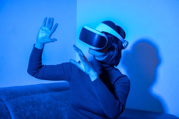 Hermosa mujer usando auriculares vr apuntando con sus manos a algo en luz azul. El concepto del universo virtual — Foto de Stock