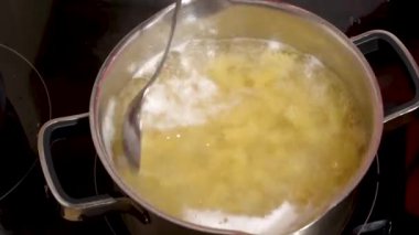 Fırının üzerindeki metal bir tencerede kaynayan suda elle karıştırılan çiğ makarna.