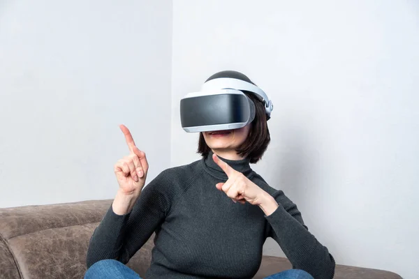 Una chica en un casco de realidad virtual señala los dedos, hace gestos de la mano en casa. El concepto del universo virtual — Foto de Stock