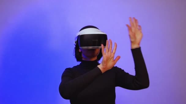 Una chica en un casco de realidad virtual extiende sus brazos como si empujara el espacio, luz de neón púrpura, hd completa. — Vídeo de stock
