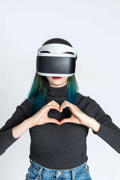 Chica adolescente usando casco vr muestra gesto del corazón con las manos en el fondo blanco. Concepto de amor virtual. El concepto de metaverso — Foto de Stock
