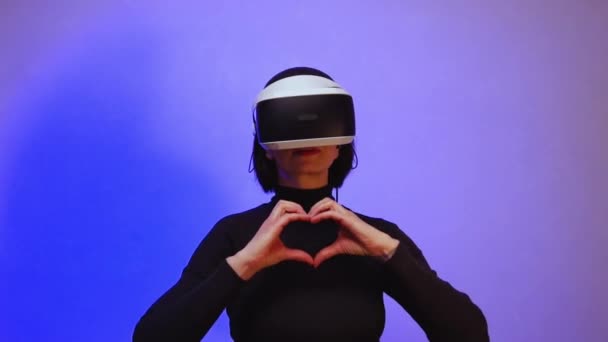 A girl in a vr helmet shows a heart with her fingers, makes a gesture with her hands in the shape of a heart, dances — Stock Video