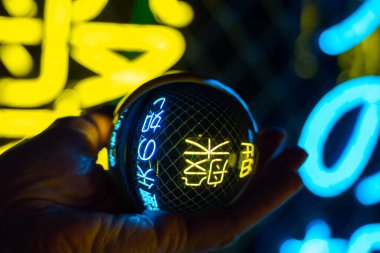 Bir el, neon ışıklarının yansımasıyla parlayan bir topu tutar. Geleceğin hikaye anlatıcısı. Paranormal yetenekler kavramı, kehanet..