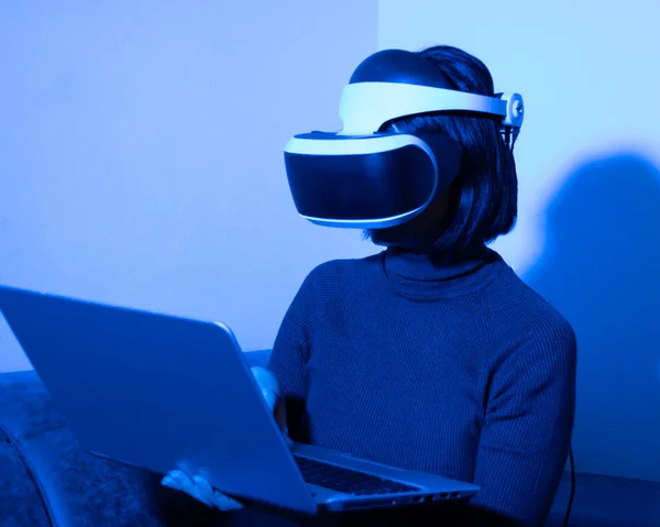 Hermosa mujer usando auriculares escribiendo en el ordenador portátil en casa en luz azul. El concepto del universo virtual. Freelancer en el espacio virtual. Concepto de éxito empresarial — Foto de Stock