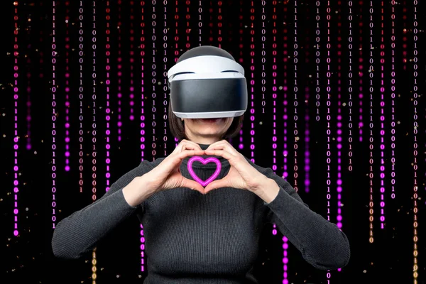 Una mujer con un casco de realidad virtual muestra con sus manos la forma de un corazón sobre un fondo púrpura de una matriz — Foto de Stock