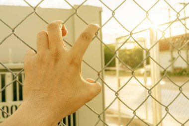 Demir ızgaradaki birinin eli umutsuz bir bekleyiş gibiydi. Demir parmaklıkları yakalama, hapsetme ya da özgürlük hissi. Yabancıların kişisel alanlara girmesini önlemek için ağ örgüsü..