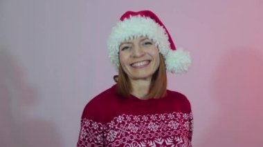 Kırmızı Noel Baba şapkalı neşeli kadın dans ediyor ve gülümsüyor.