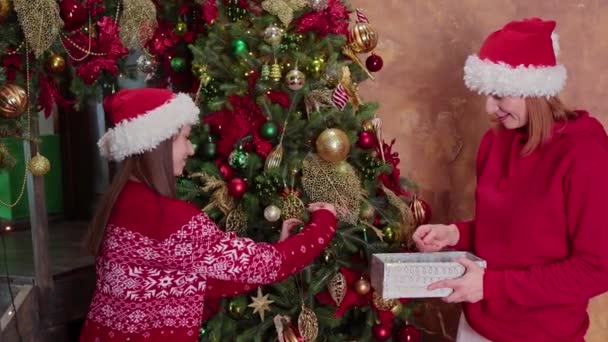 Šťastná kavkazská rodina, matka a dcera v červeném santa klobouku zdobí vánoční stromeček doma — Stock video