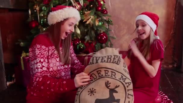 Two happy sisters sitting near New Year tree and open gifts — 图库视频影像