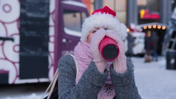 Kış kıyafetleri içinde gülen bir kadın, açık havada kırmızı bir bardak içecekle.. — Stok video