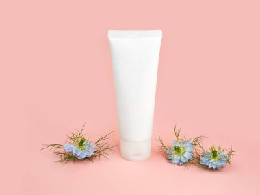 Markasız beyaz sıkılmış kozmetik krem tüpü ve pembe arka planda mavi Nigella çiçeği. Doğal orantılı spa kozmetik konsepti. Model, şablon, ön görünüm.