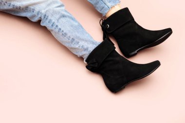 Kot pantolonlu kadın bacakları ve bej arka planda siyah kısa botlar. Boşluğu kopyala, ön üst görünüm.