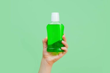 Damgalamak ve etiketlemek için yeşil sıvıyla markalaştırılmamış şişe ve yeşil arka planda erkek eli. Gargara ya da diş bakımı konsepti. Minimalizm.