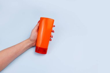 Damgasız turuncu şampuan ve markalaşma için saç kremi şişesi ve mavi arka planda kadın eli. Minimalizm, maket