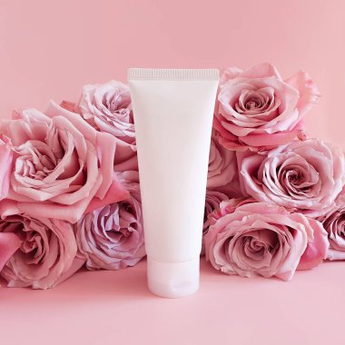 İlaç ya da kozmetik ürünlerini damgalamak için kullanılan beyaz sıkılmış plastik şişe tüpü. Krema, jöle, cilt bakımı, diş macunu ve pembe arka planda pembe güller. Biyo organik güzellik boş, ön