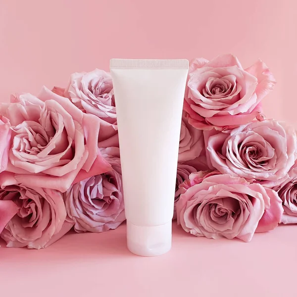 İlaç ya da kozmetik ürünlerini damgalamak için kullanılan beyaz sıkılmış plastik şişe tüpü. Krema, jöle, cilt bakımı, diş macunu ve pembe arka planda pembe güller. Biyo organik güzellik boş, ön