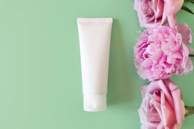 Kozmetik şişe tüpü, pembe güller ve yeşil arka planda şakayık. İlaç ya da kozmetik ürünlerini damgalamak için beyaz sıkma şişesi plastiği. Krem, nemlendirici, jöle, cilt bakımı. Boşluğu kopyala