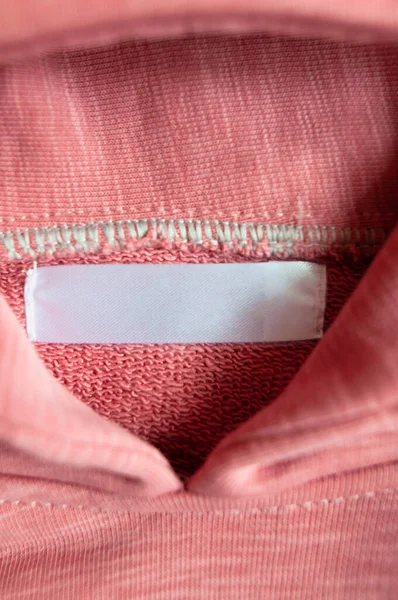 Closeup white blank clothing tag label on pink collar hoodie. Vertical photo. Selective focus.