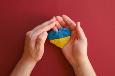 Ukrayna bayrağı, savaş yok. Kırmızı kestane rengi arka planda mavi ve sarı plastiksi kil şeklinde bir kalp. Plastik parmak dokulu arka plan. Üst görünüm, yakın plan.