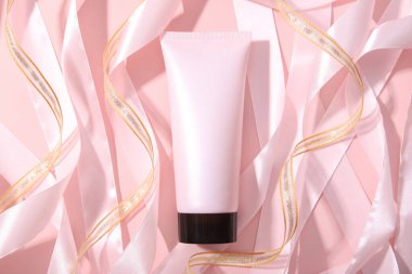 Vidalı pembe sıkma şişe kozmetik tüpü ve pembe arka planda pembe altın kurdeleler..