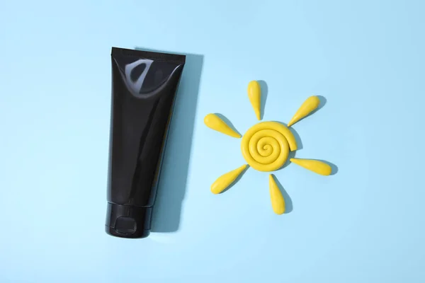 Black squeeze bottle cosmetic tube and yellow plasticine modeling clay sun on blue background with shadow. Daily cream, gel, skin care, sunscreen, moisturizer. Cosmetic blank bottle container.
