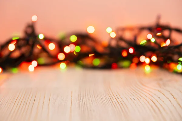 Blurred product background with Christmas New Year colorful light bulbs garland and wooden table. Selective focus, copy space for beauty product packaging, advertising backdrop. Empty place