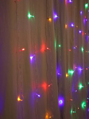LED 'in çok renkli Noel' i ya da yeni yıl çelengi bej rengi pamuk perdenin üzerinde farklı renkte ışıklar, ev dekoru. Dikey fotoğraf. Seçici odak.