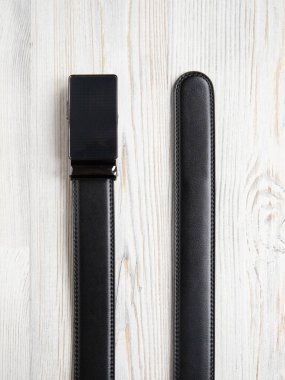 Beyaz ahşap arka planda otomatik tokalı siyah erkek deri kemerinin son parçaları. Erkek aksesuarı. Ön manzara, dikey fotoğraf, düz yatak, yakın çekim..