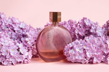 Pembe arka planda markasız kahverengi parfüm şişesi ve leylak çiçekleri. Model, markalaşma ve etiketleme için saydam cam parfüm şişesi. Eau de Tuvalet. Ön görünüm.