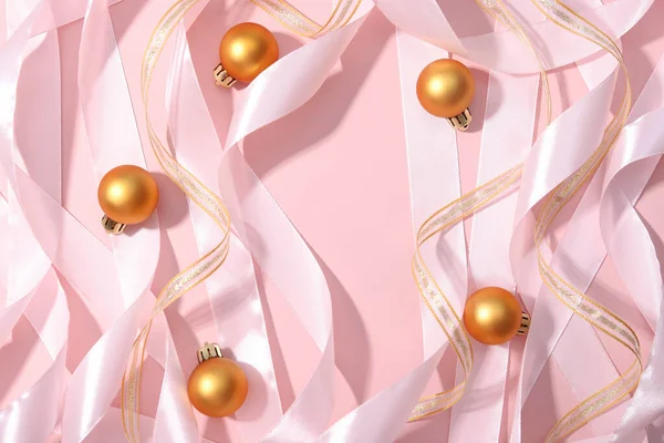 Roll pink gold ribbons and golden balls on pink background. Cosmetics product advertising backdrop. Copy space, Christmas flat lay, top view. Empty place to display product packaging, new Year party.