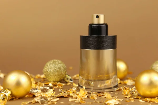 Unbranded black and gold perfume spray bottle, gold christmas balls and paper firecracker pieces on golden background. Mockup, close-up. Bottle for branding and label, front view, new Year party